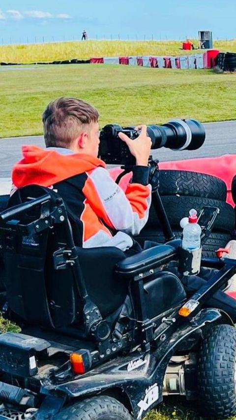 Jake Smith - man in an electric wheelchair, holding a large lens camera at a racetrack