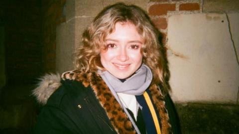 A woman with wavy blonde hair wearing a leopard print scarf.