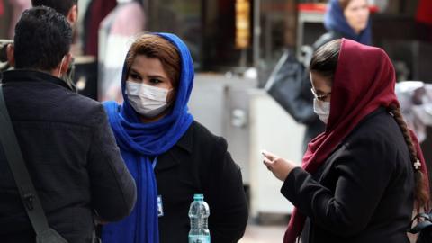 Women wearing face masks stand in a street in Tehran, Iran (26 February 2020)