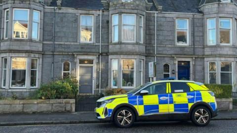 A police car parked outside a row of houses with grey stones 