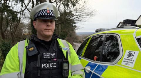 Sgt Dan Ayrton from Surrey's Roads Policing Unit, in front of a police car.