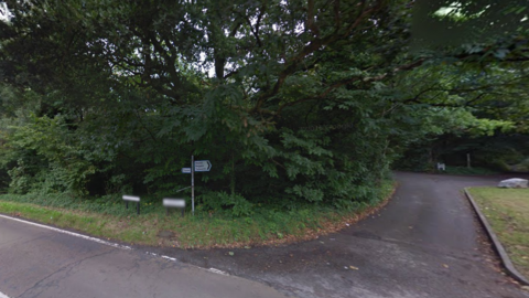 A black and white road sign at the junction of two leafy country roads in Surrey.