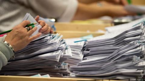 A close-up of a pile of voting papers with a pair of hands counting them