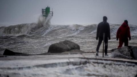 People walk as waves crash against the shore as the storm Otto arrives in Thorsminde, Denmark, February 17, 2023