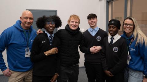 Students and teachers posing with Ed Sheeran, inside a school