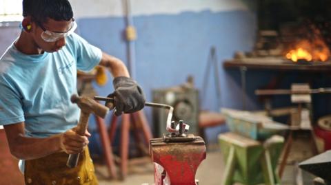 A person in Mexico working hammering a steel rod in to shape 