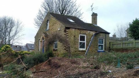 The property, which is constructed out of stone and covered in moss, in the middle of a very overgrown plot of land.