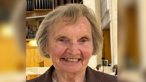 A woman is smiling at the camera with blue eyes and grey hair.