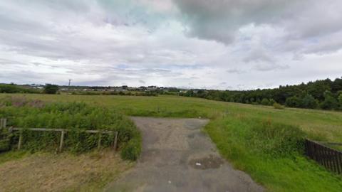 A green space in Leadgate, County Durham, where there is a proposal to build 97 new homes. It is an area of fairly wild grassland bordered by trees and hedges. A wide, concrete path leads a short way into the main field.