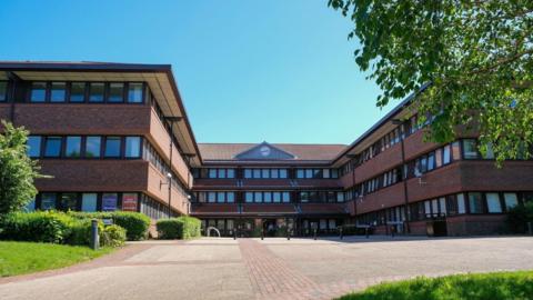 Gateshead Civic Centre. The three-storey building is red brick with rows of windows at each level. A clock has been installed above the entrance.
