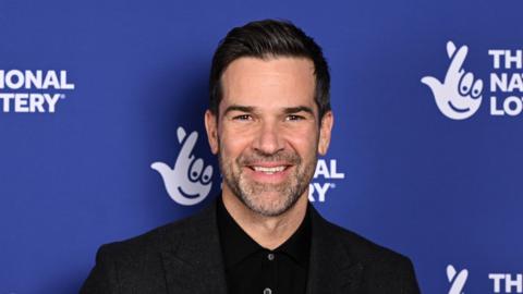 Gethin Jones, he is wearing a black shirt. He has dark brown hair and beard. 