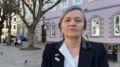 Deputy Mary Le Hegarat is wearing a black blazer and white blouse. She is pictured in Jersey's Royal Square