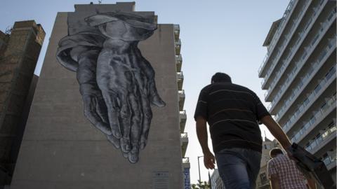 Man in Athens passes mural of praying hands