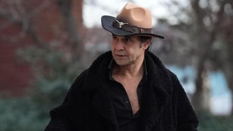 Chico arriving at court, wearing a brown cowboy hat with a silver cattle head adornment. He wears a black furry coat with a black open shirt underneath 