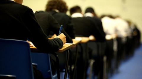 School pupils in dark uniforms doing an exam in an exam hall at individual tables 