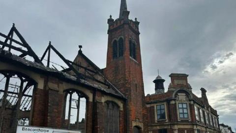 A still of a burnt-out church, as the remaining walls and window frames are black.