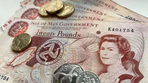 Brown and red Manx £20 notes fanned out with several Manx coins on top of them.