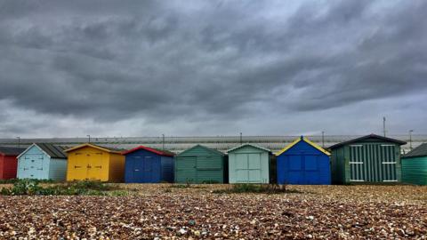 Dark clouds looming over colourful beach huts.