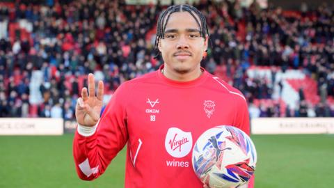 Lincoln's Jovon Makama hold three fingers up and clutches the match ball after scoring a hat-trick