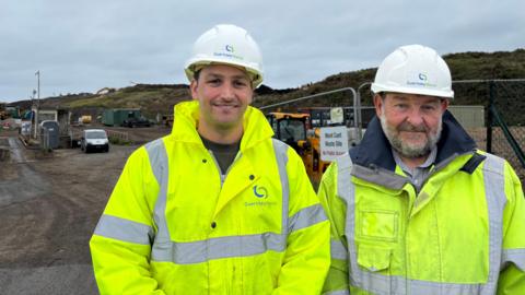 Douglas button (left) and Robert Roussel wearing green high visibility coats. Behind there are big hills. The are both wearing white Guernsey Waste hats.