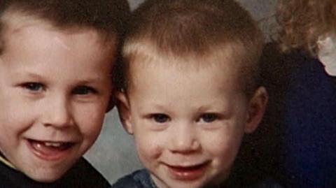 A 1990s picture of two young boys, aged around eight and six. They are both blond and smiling into the camera.