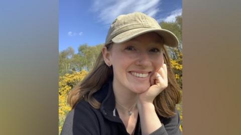 Photograph of Lily Sparrow. She has shoulder length brown hair and is wearing a baseball cap