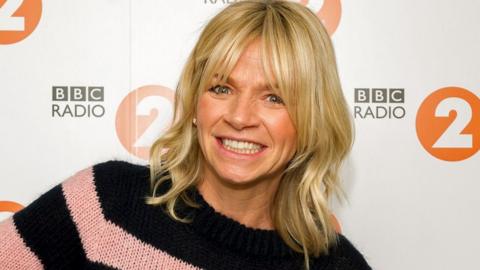 Zoe Ball posing in front of a backdrop showing BBC Radio 2 logos