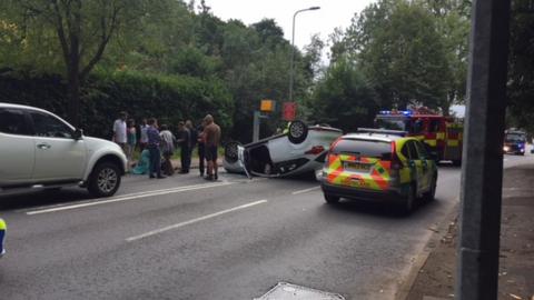 An overturned car and police and fire engine arriving