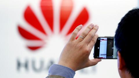 A man takes a photograph of Huawei logo