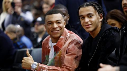 Kylian Mbappe sits courtside with his brother Ethan Mbappe
