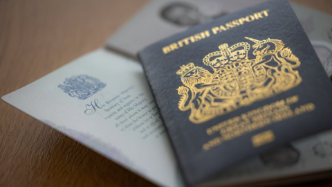 A British passport laid on a table on top of another open passport. The cover is dark blue and gold.