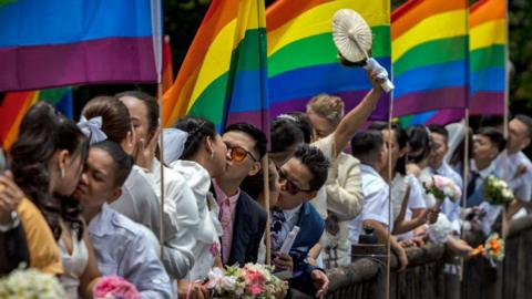 Same-sex couples kiss with LGBT rainbow flags in the background