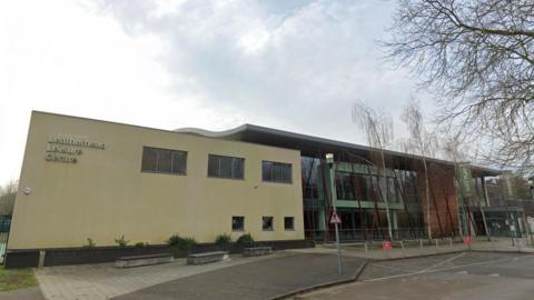 The outside of a leisure centre, the left half is painted cream, while the right half is brick and glass