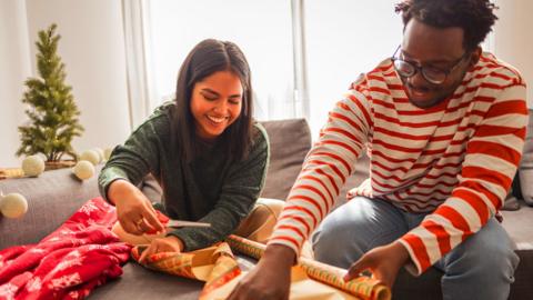 A smiling young man and woman wrap presents together