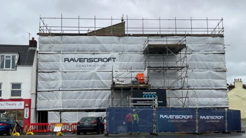 The exterior of the Coop Longstore in Guernsey. It has scaffolding around it, and white covers.