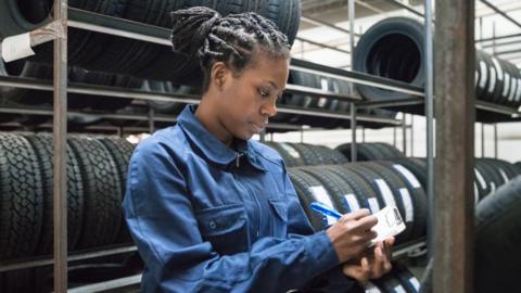 Woman writing on a clipboard, standing between rows of tyres