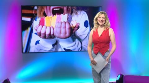 Jenny in the studio with a child eating cake in the screen