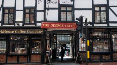 The entrance to The George Hotel is displayed via a red sign hanging above an entrance way off a street.
