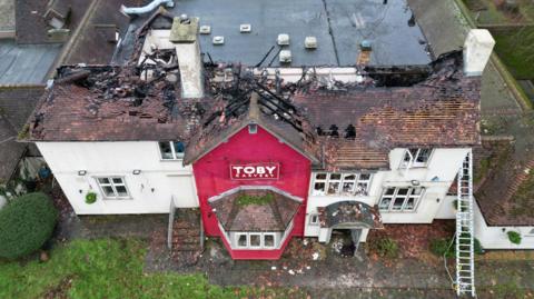 An aerial view of a Toby Carvery building, which is blackened and fire-damaged.