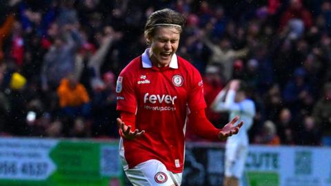 Sam Bell holds his hands in front of him with his palms up and has his eyes tightly closed as he runs in celebration after scoring