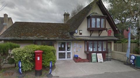 A view of the Post Office in Foxton. The small building has brown bay windows and a red post box outside.