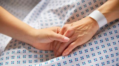 Two people hold hands on top of a patterned hospital gown. 