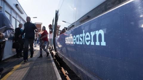 Passengers alight from a Southeastern train at a station, with the train painted in its blue and white livery.