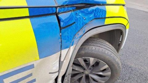 A close up image of a police vehicle shows dents to the front bumper. 