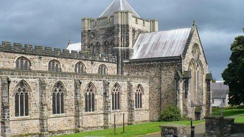 Cathedral in light grey stone with vaulted windows and tower seen at one end