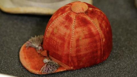 A tiny red cap from the 19th century with two tassels on its front.