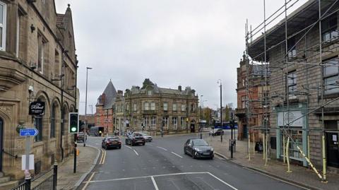 The A666 Bolton Road in Darwen town centre showing vehicles travelling on the road with buildings including pubs and shops