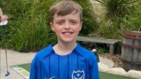 Beau Croucher wearing a blue Portsmouth Football shirt and smiling at the camera in a crazy golf course.
