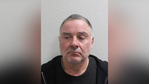 Custody image of Thomas McKenna, wearing a dark top, photographed against a plain wall.