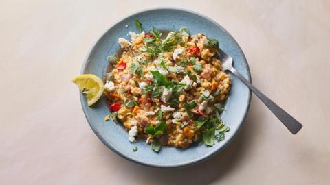 Mediterranean no stir risotto in a blue bowl on a light peach background.